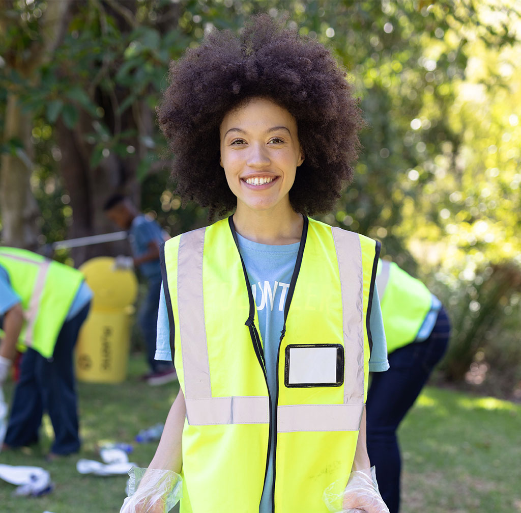 Smiling woman in reflective vest volunteering outdoors.